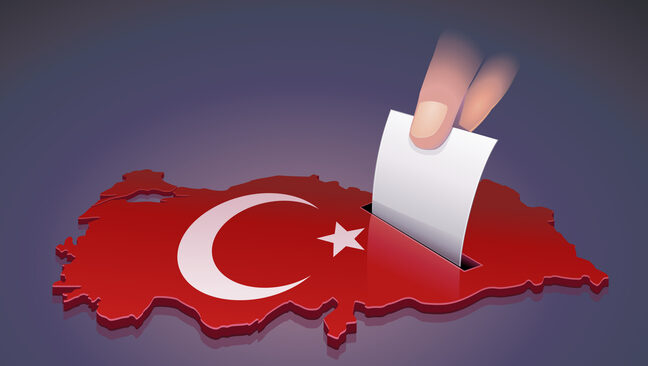 Hand dropping a ballot into a slot on the 3D map of Turkey in the colors of the Turkish flag symbolizing an election in Turkey on dark background